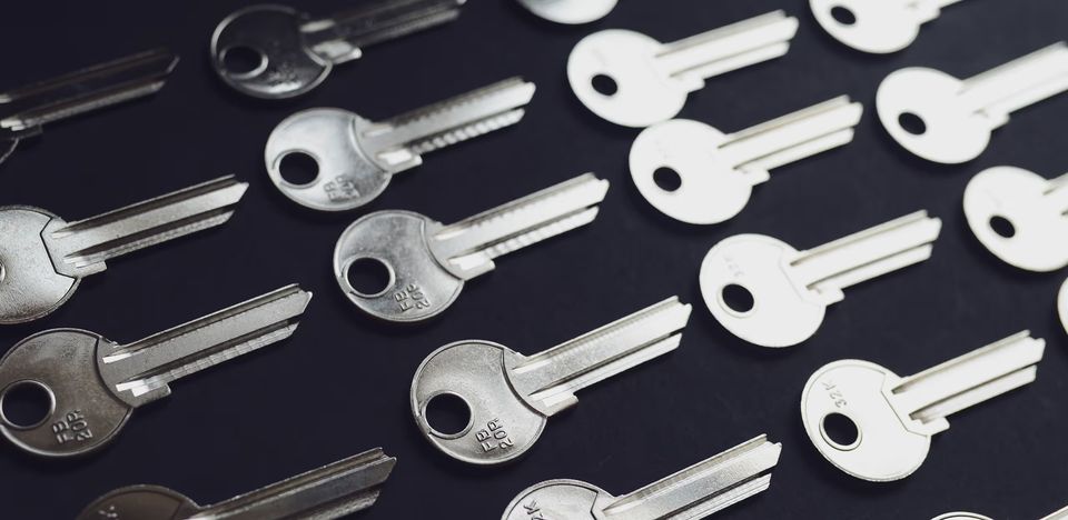 The image depicts several identical silver keys arranged in orderly rows against a dark background. The image depicts several identical silver keys arranged in orderly rows against a dark background.